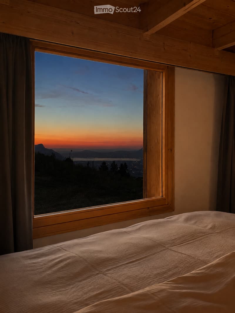 Cozy bedroom with a large window showcasing a scenic sunset view over a landscape, featuring a neatly made bed.