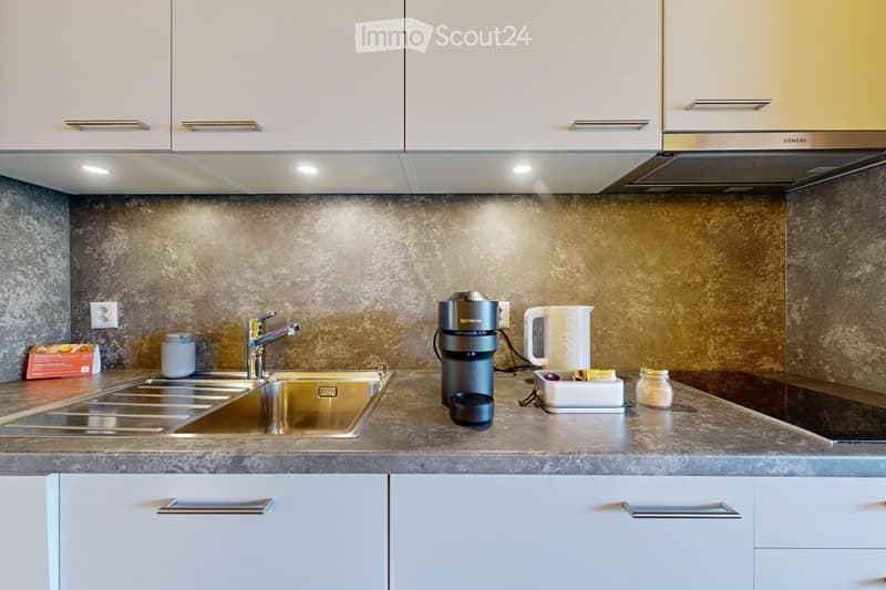 Modern kitchen with white cabinets, stainless steel sink, coffee maker, kettle, and various small appliances on the counter.