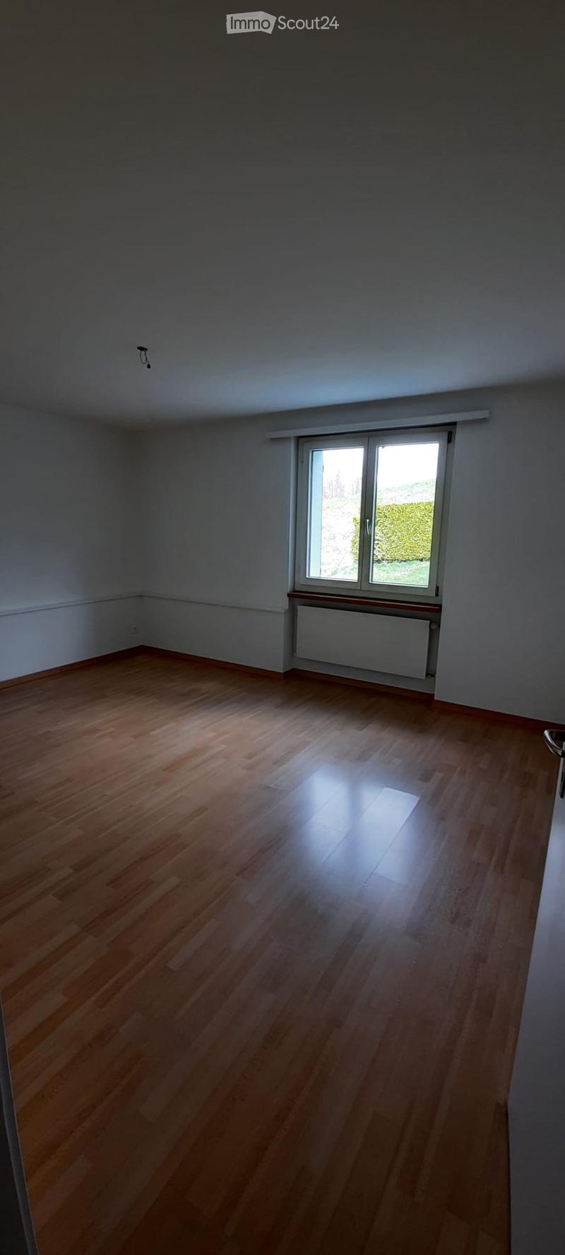 Empty room with wooden flooring, white walls, and a large window with blinds. No furniture or equipment present.
