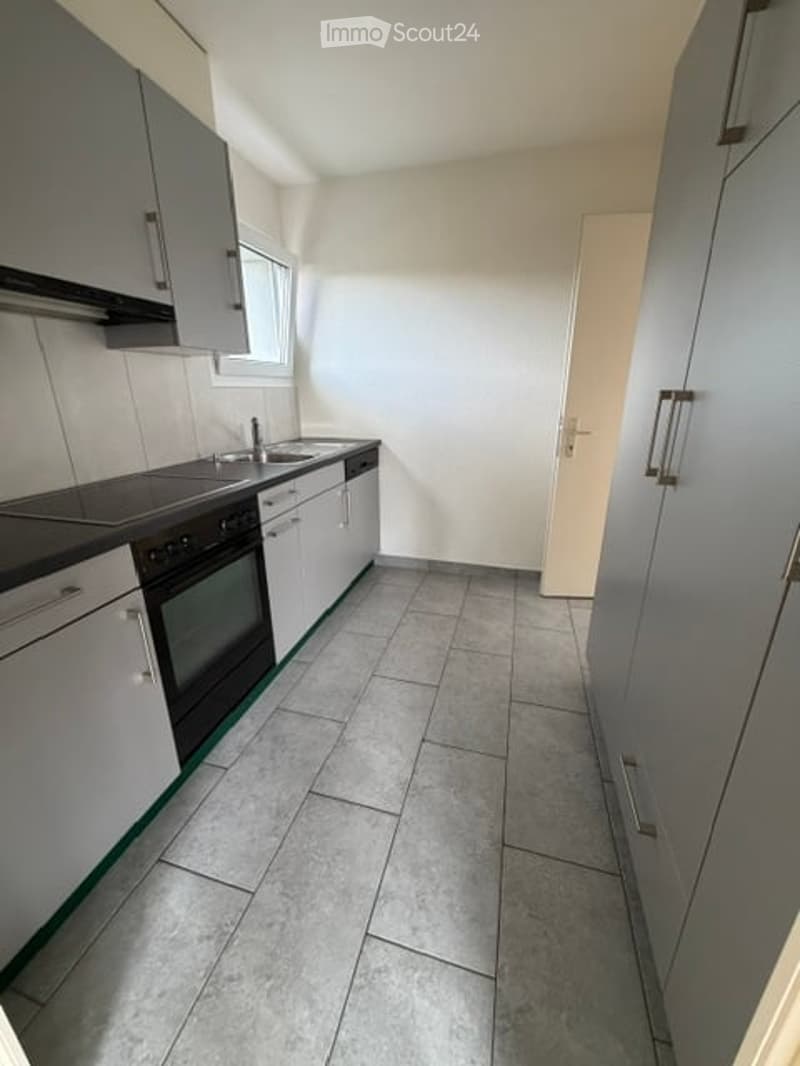 Modern kitchen with white cabinets, black countertop, and grey tiled floor. Includes a sink, faucet, oven, and dishwasher.