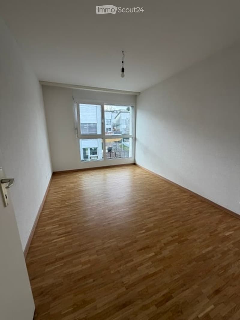 Empty room with wooden flooring, white walls, and a large window with a view of the outside.