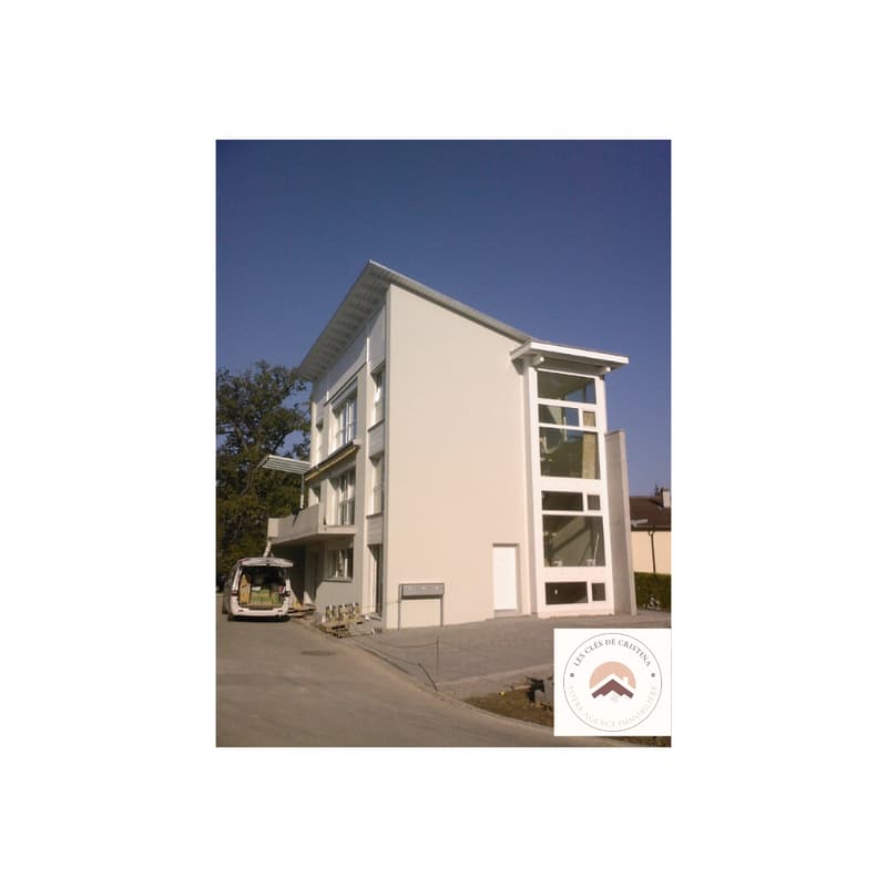 Modern two-story building with white exterior, large windows, and a balcony on the upper level.