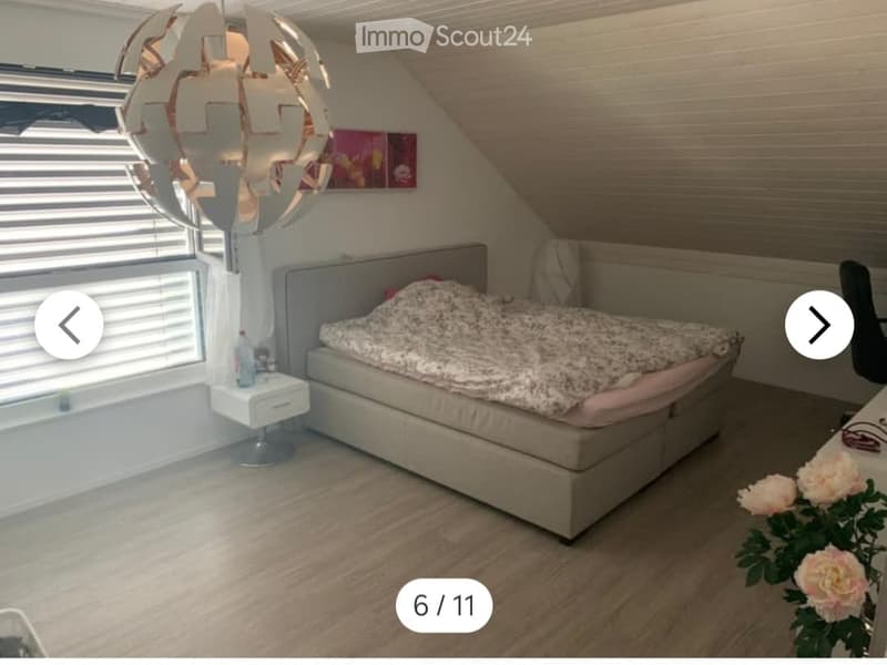 Cozy bedroom with a large bed, nightstand, and decorative floor lamp. The room features wooden flooring and large windows with blinds.