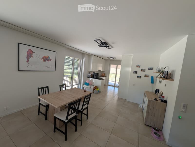 Bright dining area with a wooden table and chairs, white kitchen cabinets, balloons, and a framed picture on the wall.