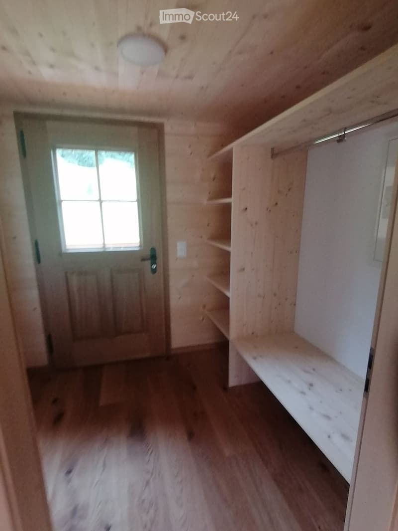Empty room with wooden walls, wooden floor, built-in shelves, and a window with multiple panes.