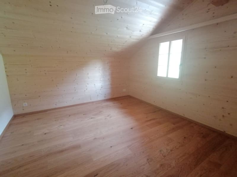 Empty room with wooden flooring and exposed wooden ceiling beams. Single window on one wall, no furniture or decorations.
