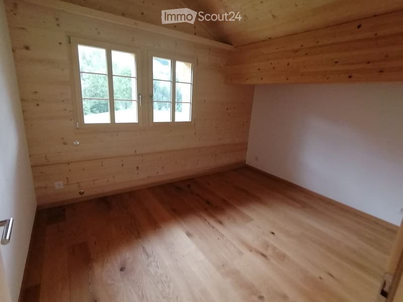 Empty room with wooden walls, wooden floor, and large windows letting in natural light.