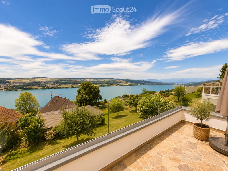 Balcony with a view of a lake and surrounding landscape, featuring a table, umbrella, and potted plant.