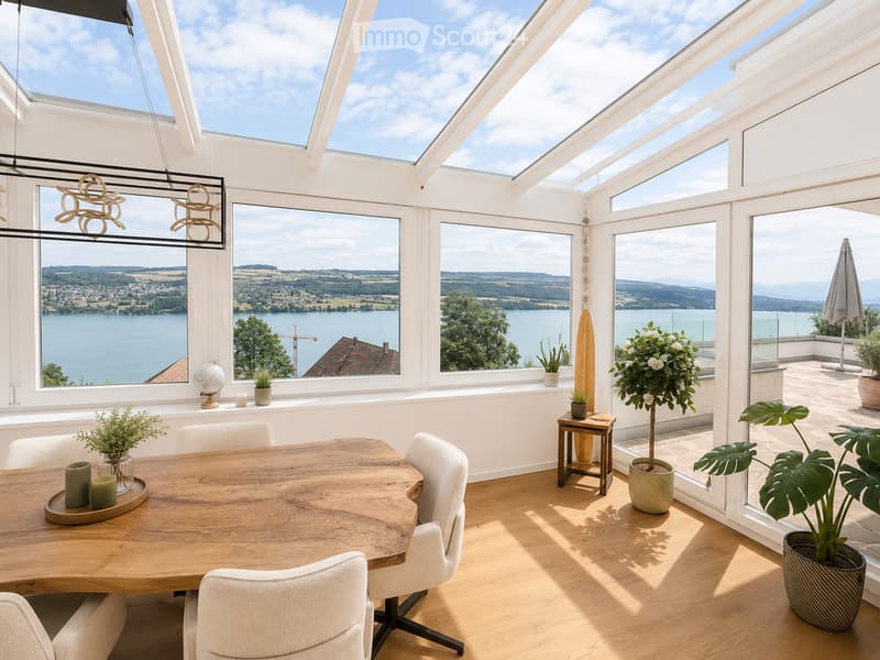 Bright, airy dining area with large windows offering scenic views, featuring a wooden dining table, chairs, potted plants, and decorative items.