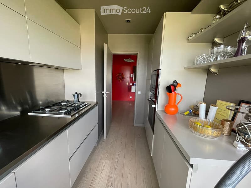 Modern kitchen with white cabinets, stainless steel appliances, and a light wooden floor. The counter features a glass bowl, a decorative pitcher, and a few other small items.