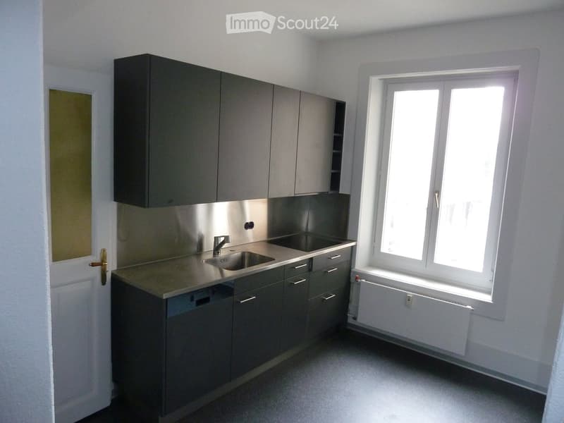 Modern kitchen with grey cabinets, stainless steel sink, and a window providing natural light.