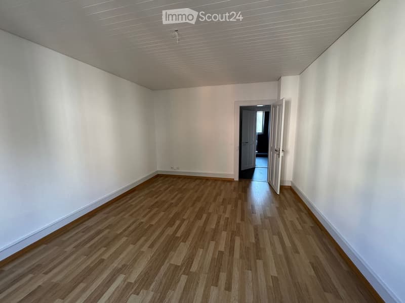 Empty room with light wooden flooring and white walls, featuring an open doorway leading to another space.