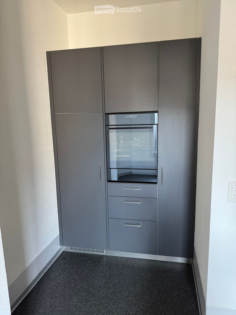 Modern kitchen with grey cabinets, built-in oven, and black tiled floor.