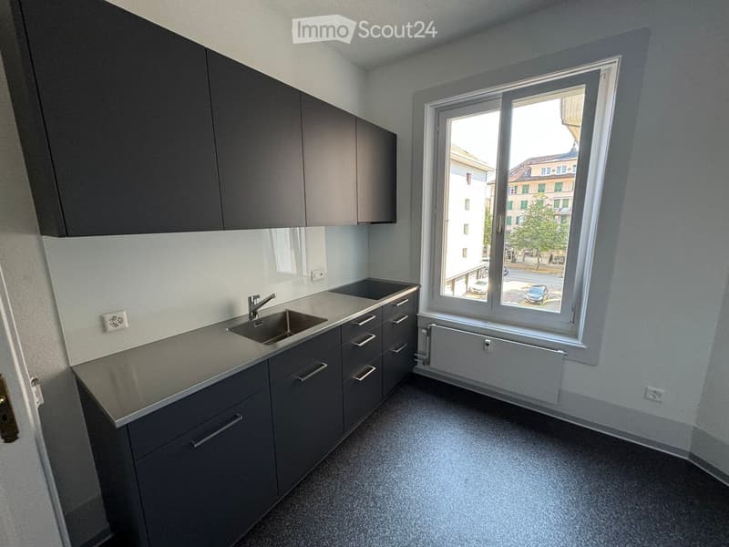 Modern kitchen with grey cabinets, a sink, and a window overlooking a street with parked cars.