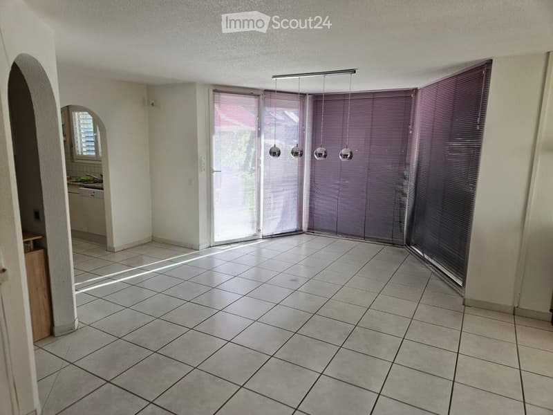 Empty room with tiled floor, white walls, and purple blinds on large windows. A small wooden cabinet is visible in the corner.