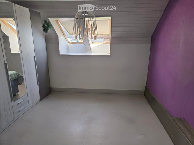 Empty hallway with carpeted floor, slanted ceiling, large skylight window, and a mirrored wardrobe on the left side.
