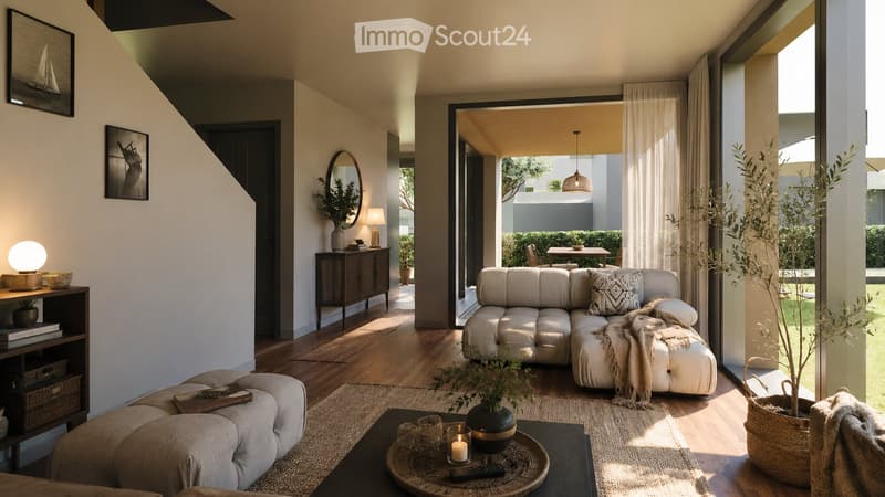 Modern living room with a light grey sectional sofa, coffee table, floor lamp, side table, mirror, bookshelf, and potted plants. The space features large windows and a view of an outdoor area.
