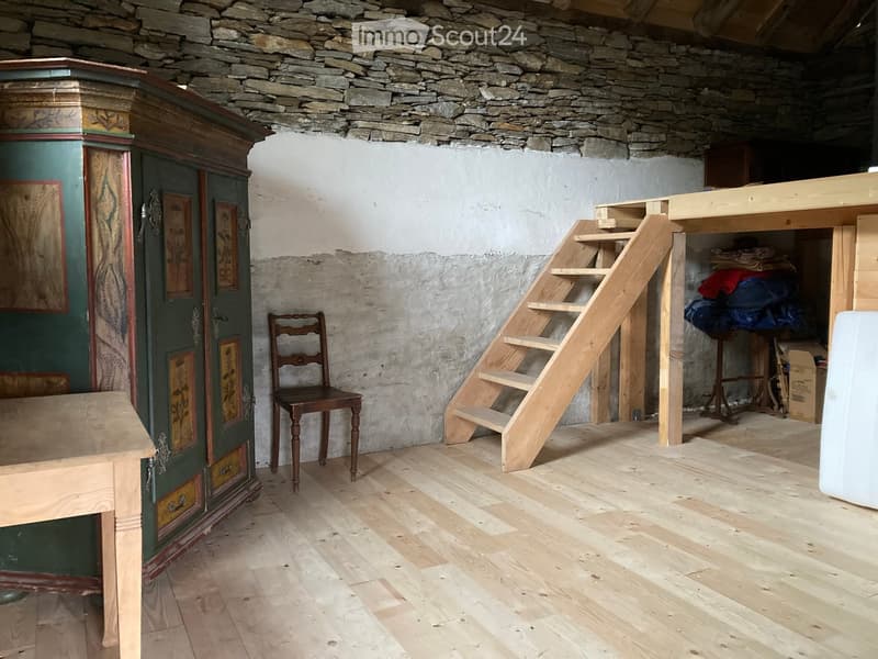 A room with wooden flooring, a staircase leading to a loft area, a wooden chair, and a large green wardrobe with floral designs.