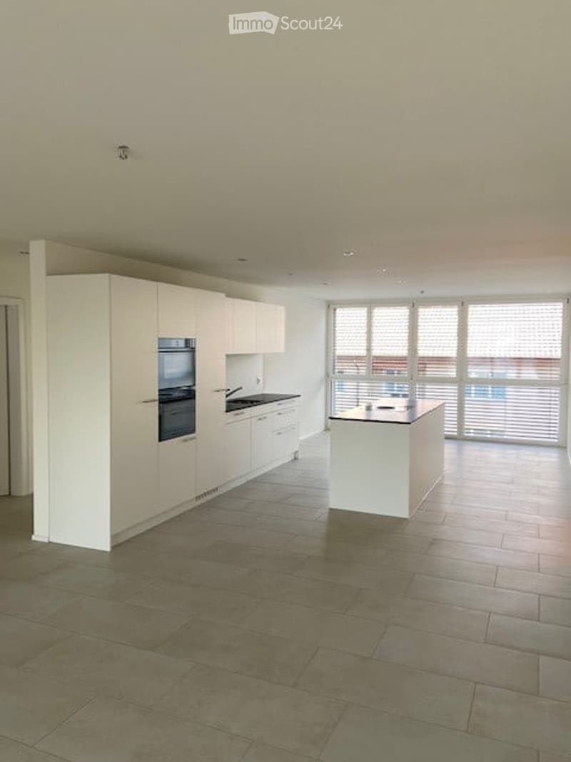 Modern kitchen with white cabinetry, built-in oven, island, and large windows offering a view.