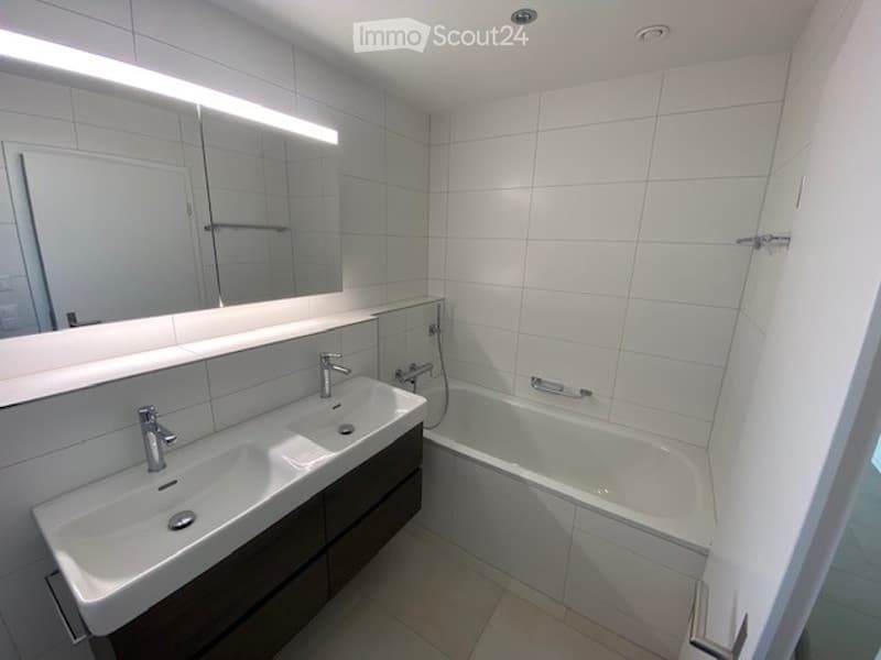 Modern bathroom with white tiles, double sink, bathtub, and large mirror with built-in lighting.