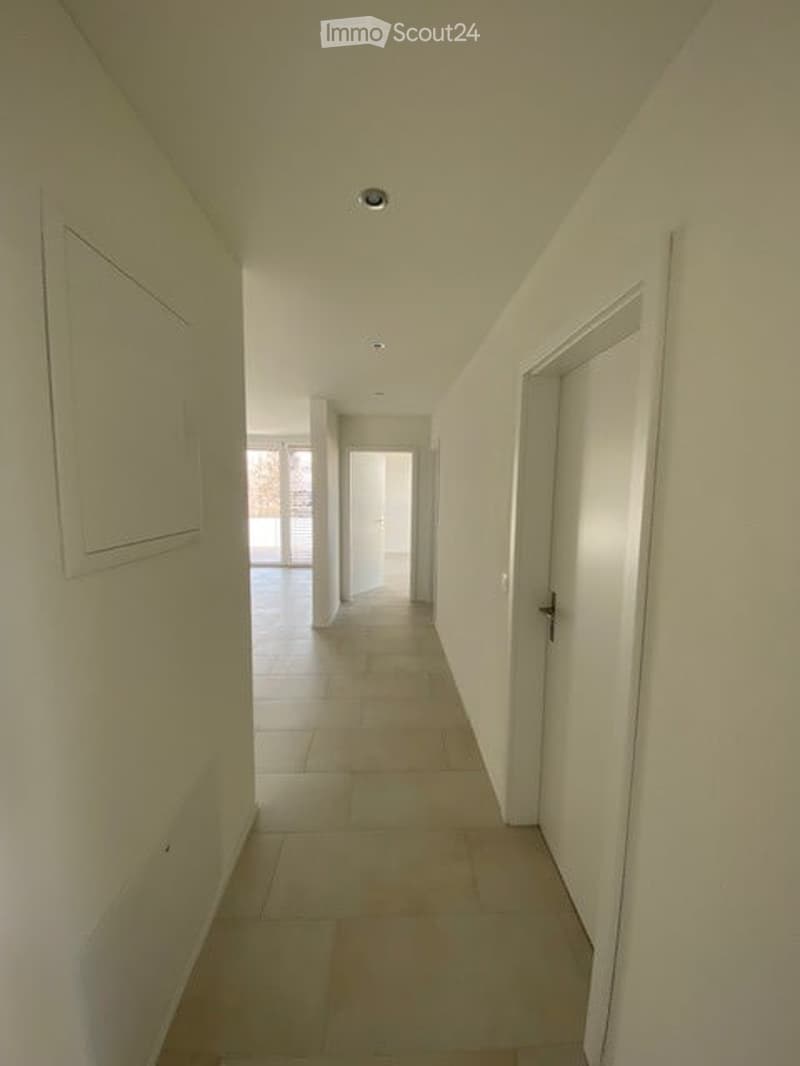 Empty hallway with white walls, tiled floor, and several closed doors leading to other rooms.