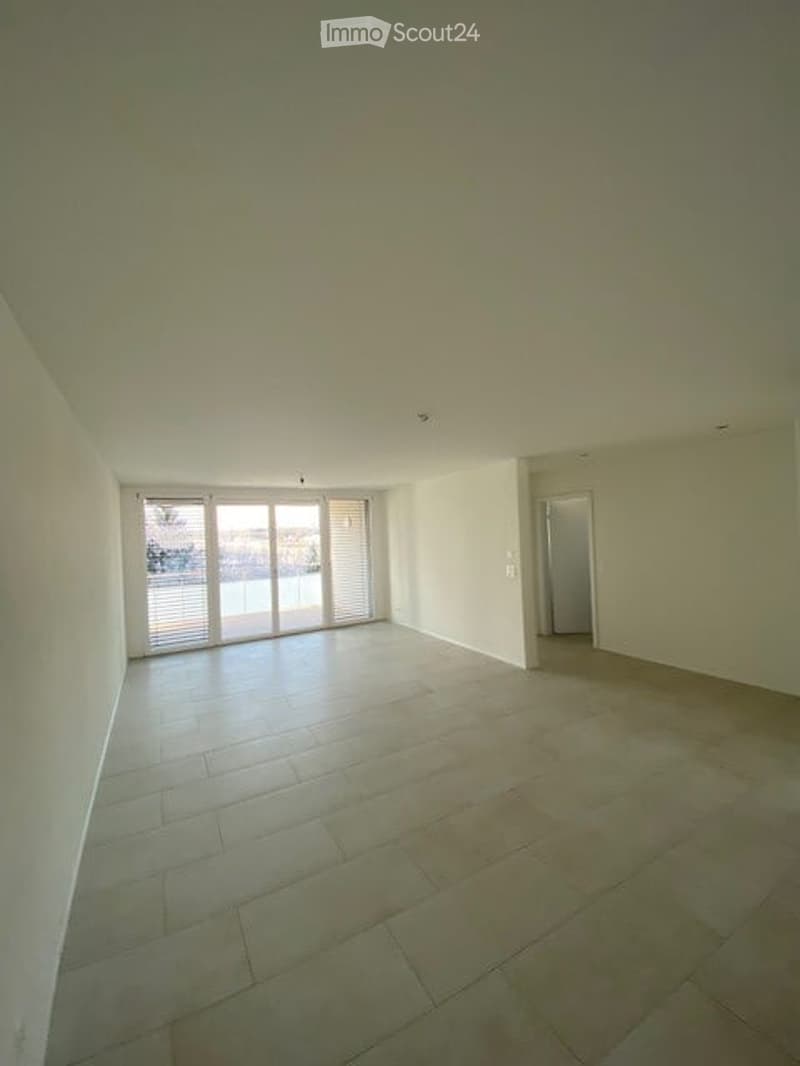 Empty room with tiled floor, white walls, large sliding glass doors leading to an outdoor area, and a doorway to another room.