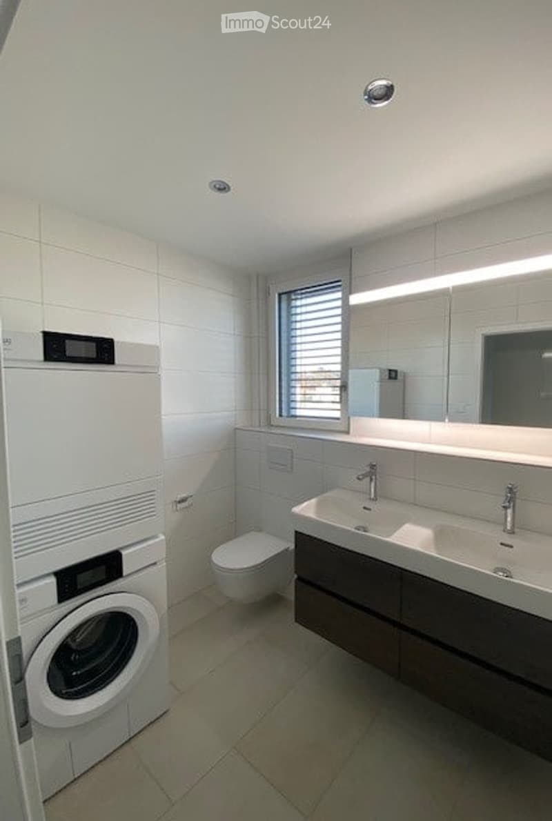 Modern bathroom with a double sink, large mirror, toilet, and a private washing machine.