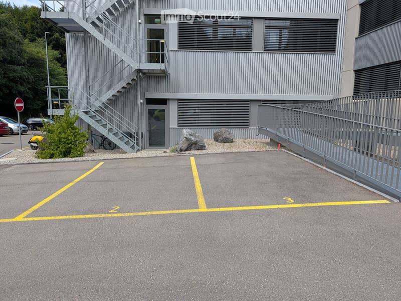 Modern industrial-style building with a metal facade, external staircase, and designated parking spaces marked with yellow lines.
