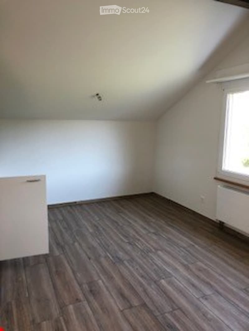 Completely empty room with wooden flooring, white walls, and a window on one side. No furniture or equipment is present.