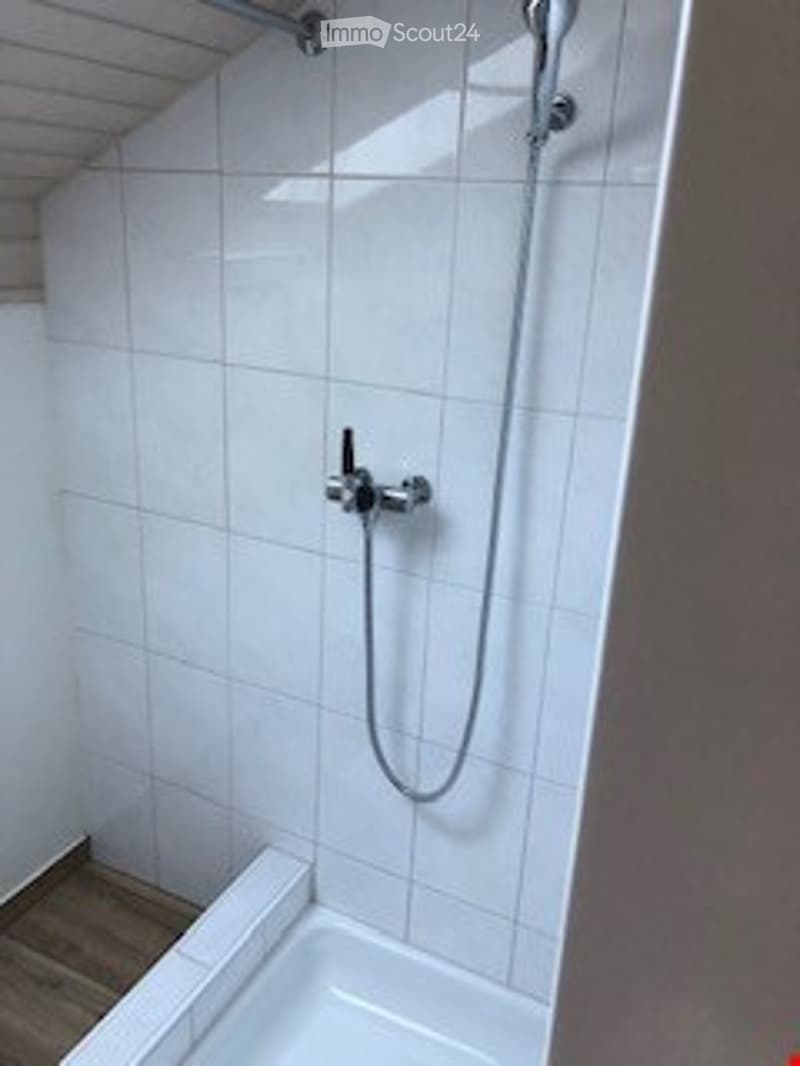 Modern bathroom with white tiled walls and floor, a showerhead, and a faucet.