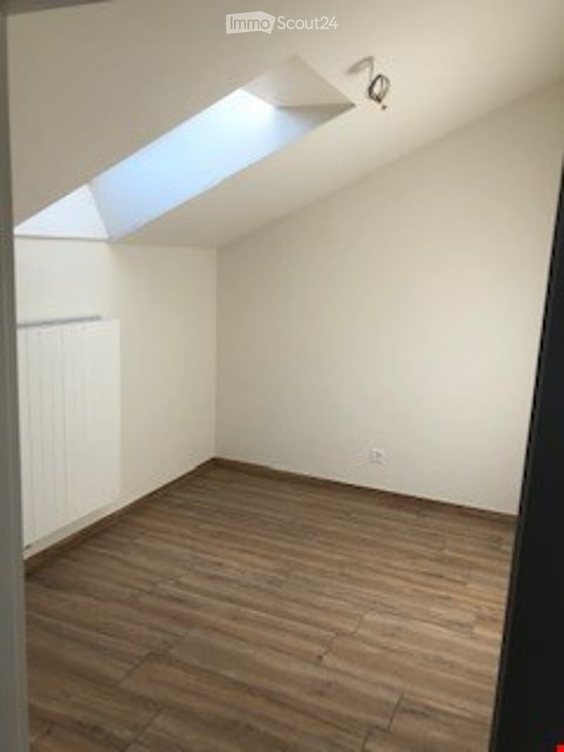 Completely empty attic room with wooden flooring, white walls, and skylight windows.