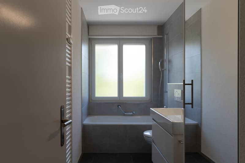 Modern bathroom with a bathtub, sink, and toilet, featuring large windows and sleek, contemporary design.