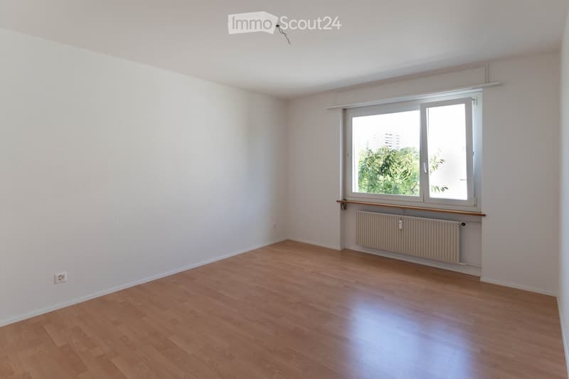 Empty room with wooden flooring, white walls, and a large window with a radiator below it.