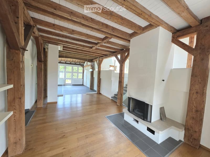 Spacious hallway with exposed wooden beams and polished wooden flooring, featuring a modern white fireplace with a black insert and a staircase leading upwards.