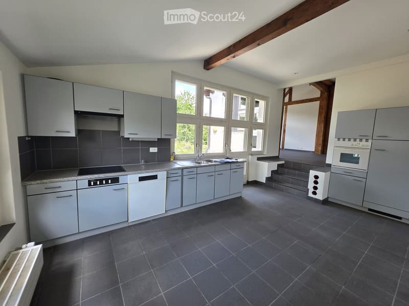 Modern kitchen with grey cabinets, dark tiled backsplash, granite countertop, stainless steel sink, and built-in appliances including an oven and refrigerator.