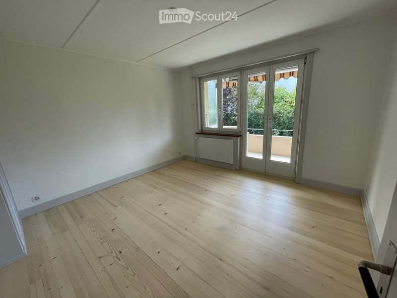Empty room with light wooden flooring, white walls, large sliding glass doors leading to a balcony, and a radiator under one window.