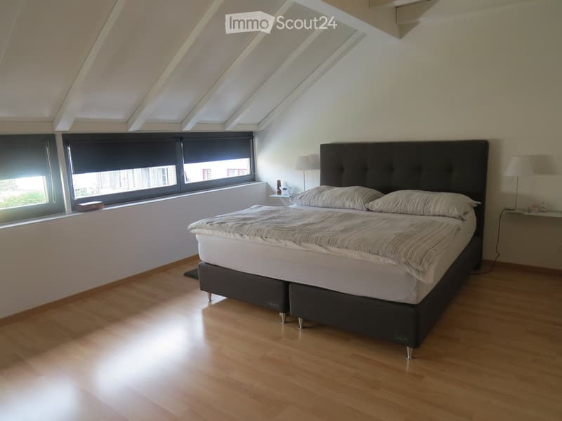 Bright bedroom with wooden flooring, large window with blinds, double bed with headboard, nightstands, and lamps.