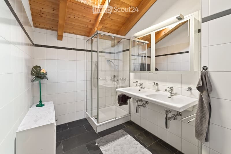 Modern bathroom with white tiles, double sink, large mirror, glass-enclosed shower, and decorative plant on a marble shelf.