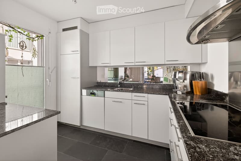 Modern kitchen with white cabinets, granite countertops, stainless steel appliances, and a large window with a view of greenery.