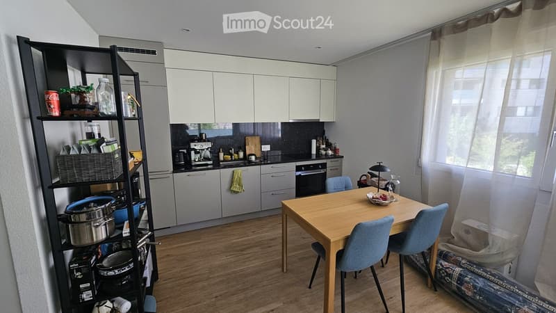 Modern kitchen with white cabinets, wooden floor, dining table with chairs, and various kitchen appliances and utensils.