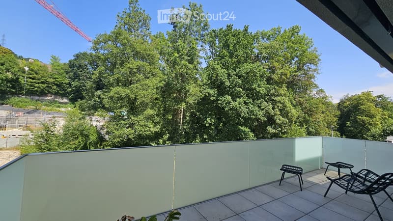 Balcony with modern glass railing, tiled floor, and outdoor furniture including chairs and a small table.