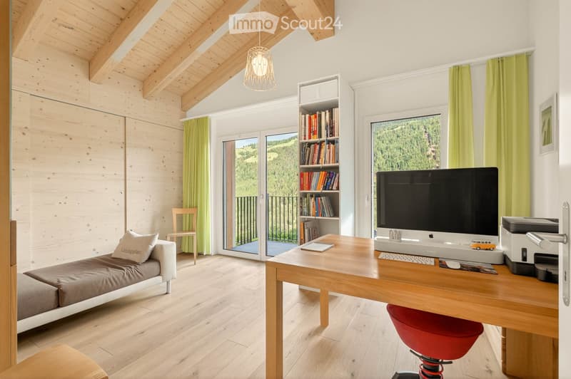 Bright, modern room with wooden beams, large windows offering a scenic view, a comfortable sofa, a desk with a computer setup, and a bookshelf filled with books.