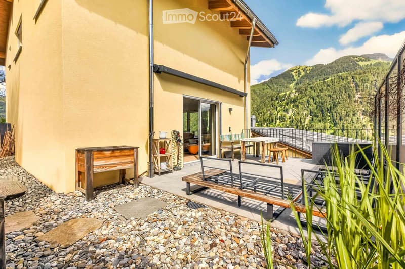 Outdoor patio area with wooden bench, table, chairs, and a view of the mountains.