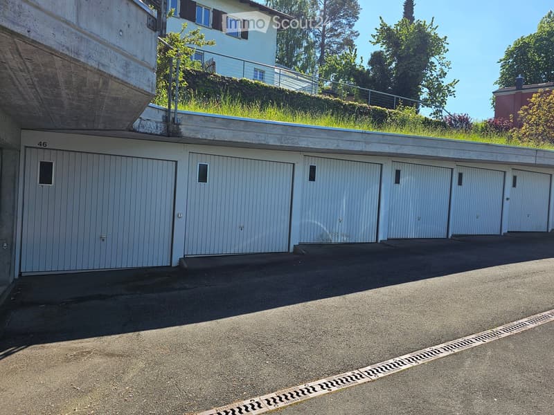 A multi-car garage with several closed garage doors, located under a raised ground floor with a grassy roof area and a staircase leading up to a house.
