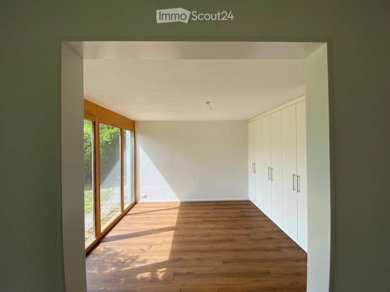 Empty room with wooden flooring, white walls, built-in white cabinets, and large glass sliding doors leading to an outdoor area.