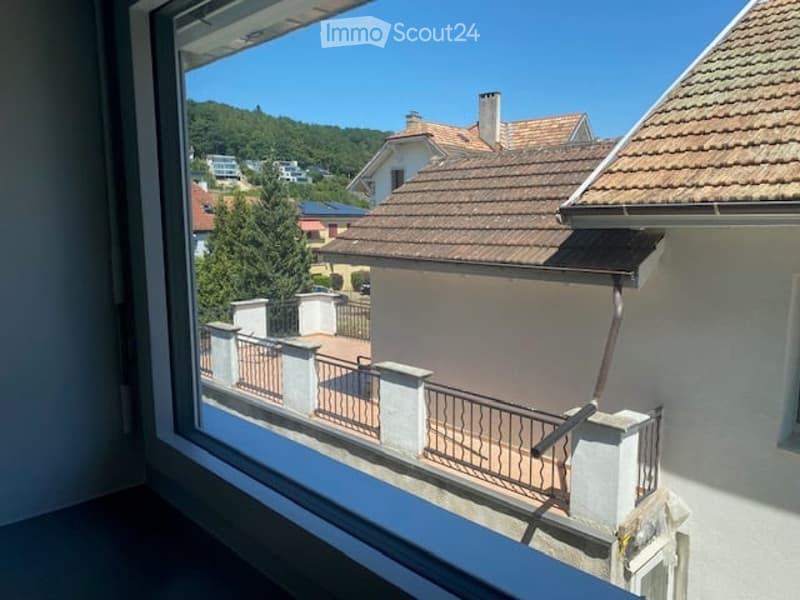 Balcony with metal railing, overlooking a residential area with houses, trees, and a clear blue sky.