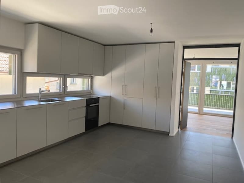 Modern kitchen with grey cabinets, stainless steel sink, oven, and a view to a balcony.