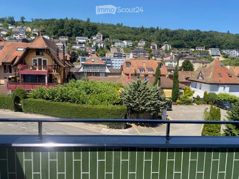 Balcony overlooking a town with houses, trees, and a clear blue sky.