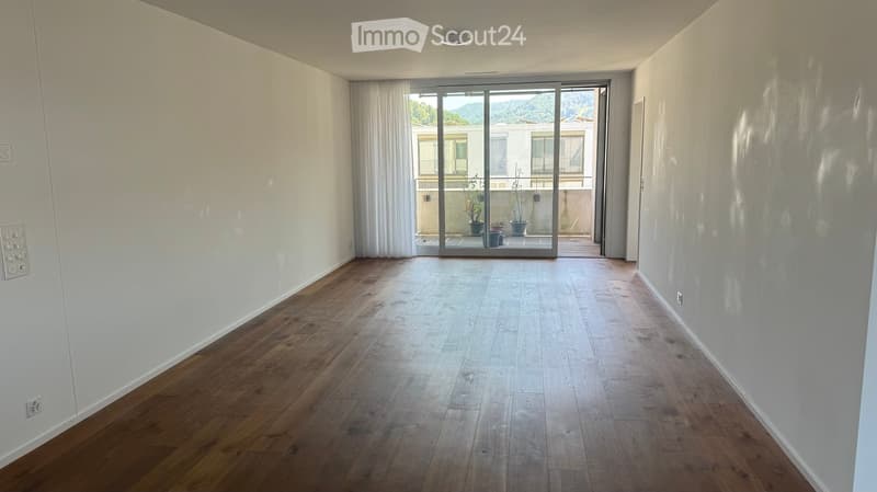 Empty room with wooden flooring, white walls, and large sliding glass doors leading to a balcony.