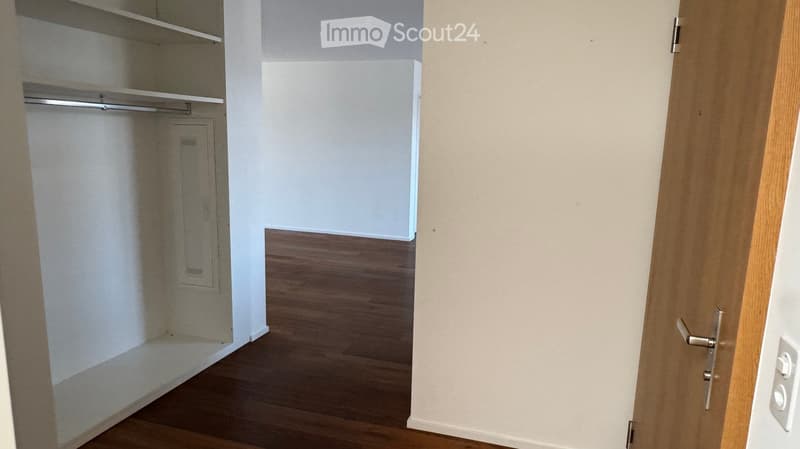 Empty room with wooden flooring, white walls, and built-in closet with empty shelves and a hanging rod.